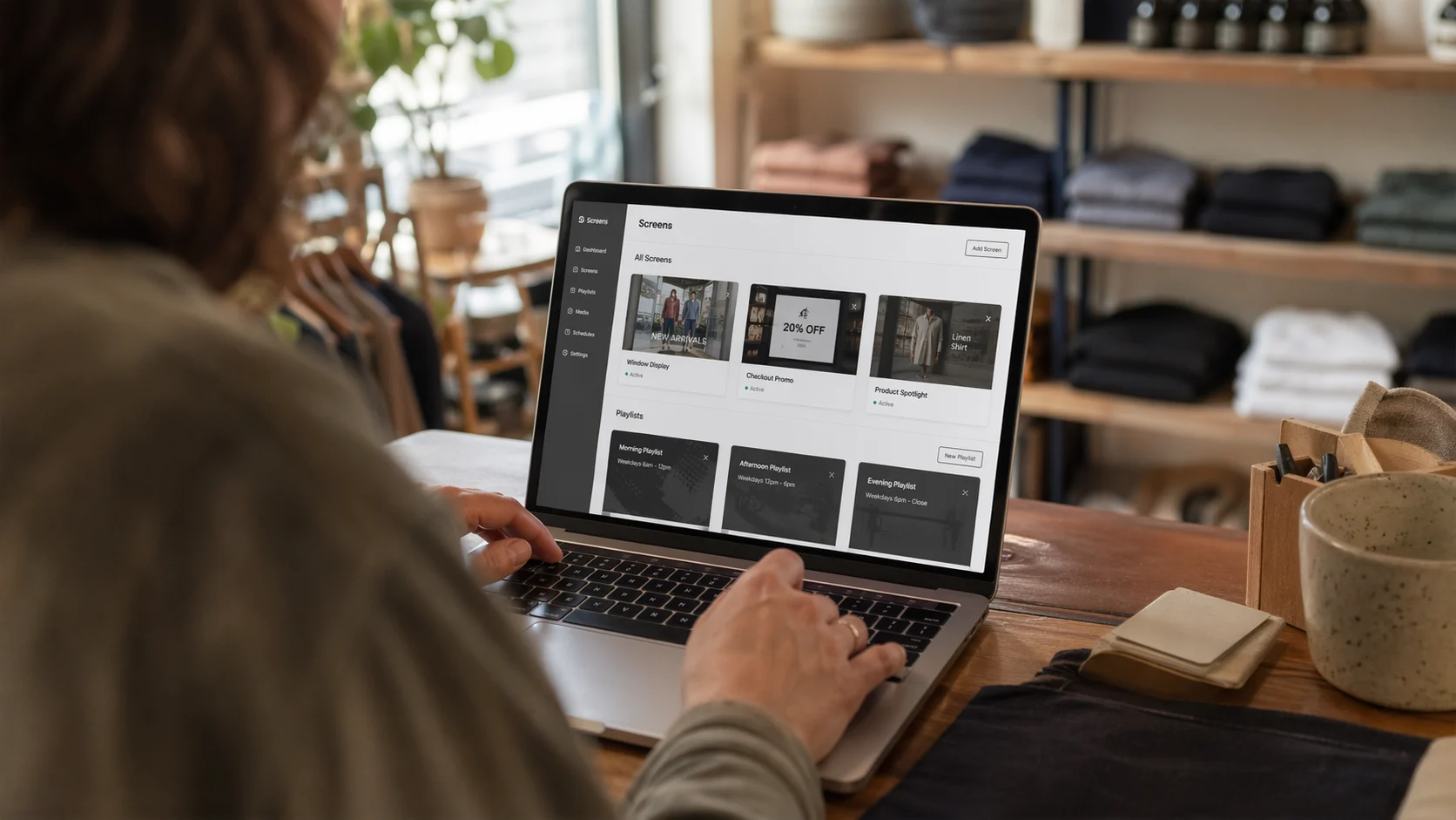 Shop owner using a laptop to manage digital signage playlists for window, checkout, and product spotlight screens